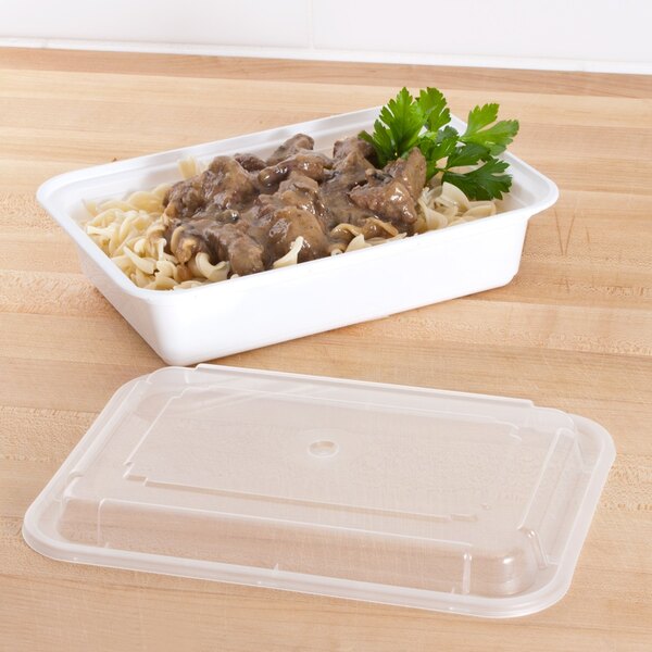 A white Pactiv rectangular microwavable container with noodles and meat in it.