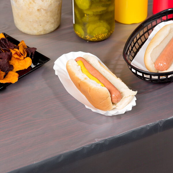 A hot dog in a bun on a white table cover with a basket of chips.