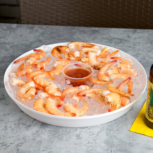 A white plastic bar tray holding a plate of shrimp and a bottle of beer on a table.