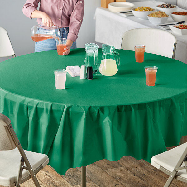 A person pouring orange liquid into a cup on a table with an Emerald Green OctyRound table cover.