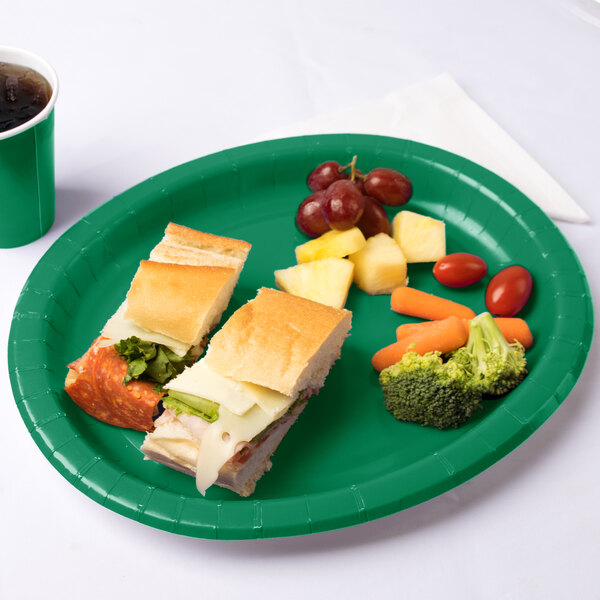 An oval emerald green paper platter with a sandwich and fruit on it.