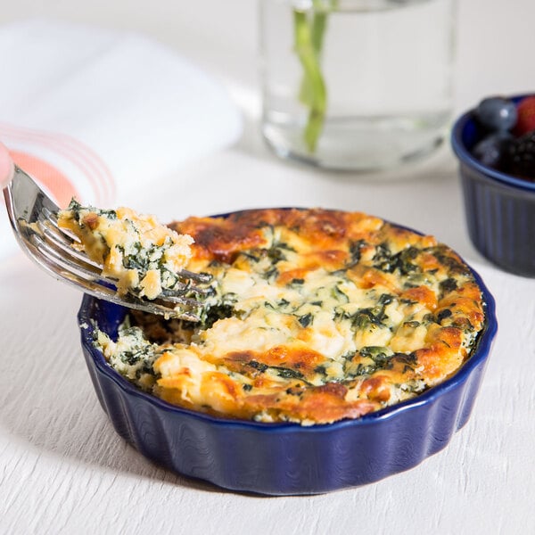 A fork in a blue CAC Festiware quiche dish with spinach and cheese.