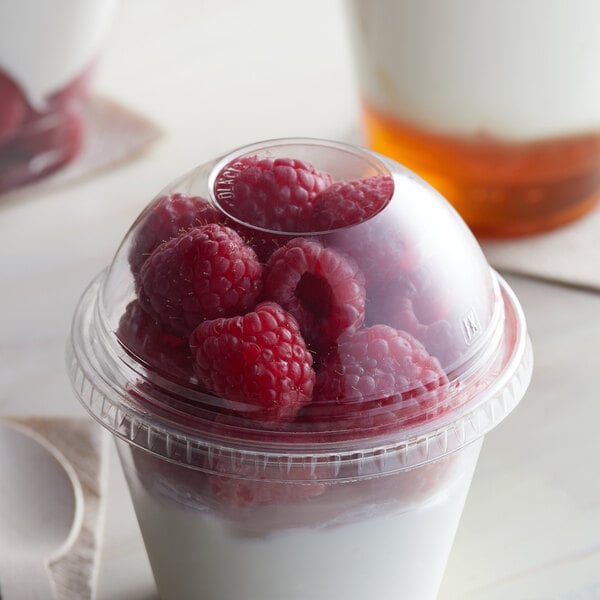 A Fabri-Kal clear plastic dome lid on a cup of yogurt with raspberries.