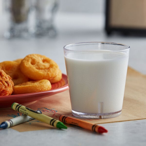 A clear plastic GET tumbler filled with milk on a table next to a plate of food.