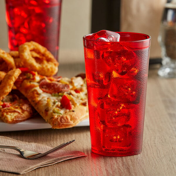 A red drink in a GET red plastic tumbler with ice on a table with pizza.