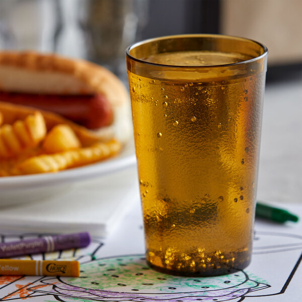 An amber plastic pebbled tumbler filled with beer next to a plate of a hot dog and fries.