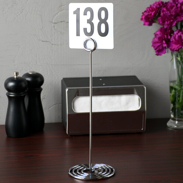 An American Metalcraft Chrome Swirl Base Card Holder with a number on a table.