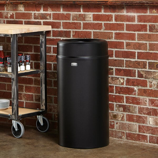 A Rubbermaid black round open top trash can with a rigid plastic liner.