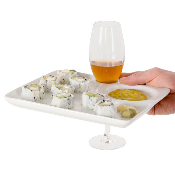 A hand holding a CAC square party plate with sushi and a wine glass.