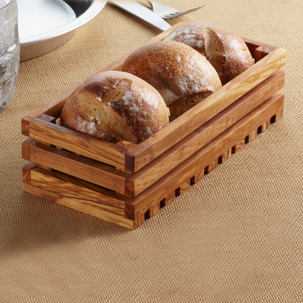 An American Metalcraft olive wood bread crate on a table with a loaf of bread inside.