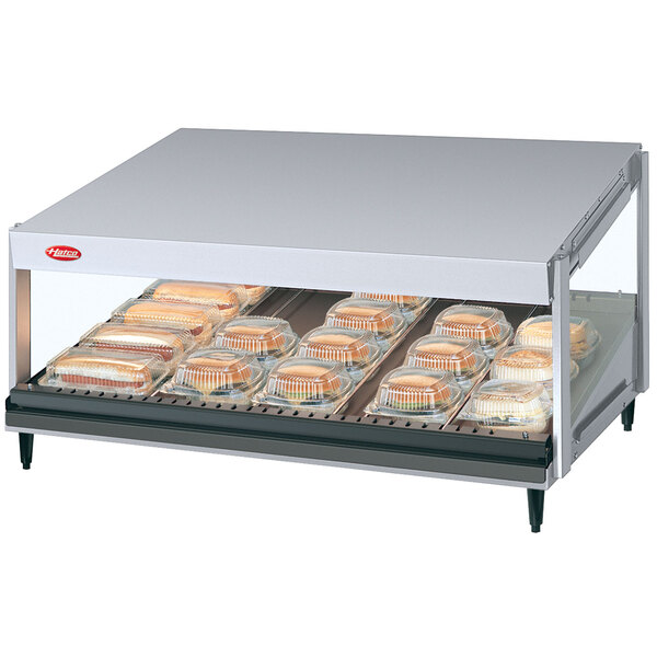 A Hatco White Granite slanted shelf countertop food warmer with food on a tray in a glass case.