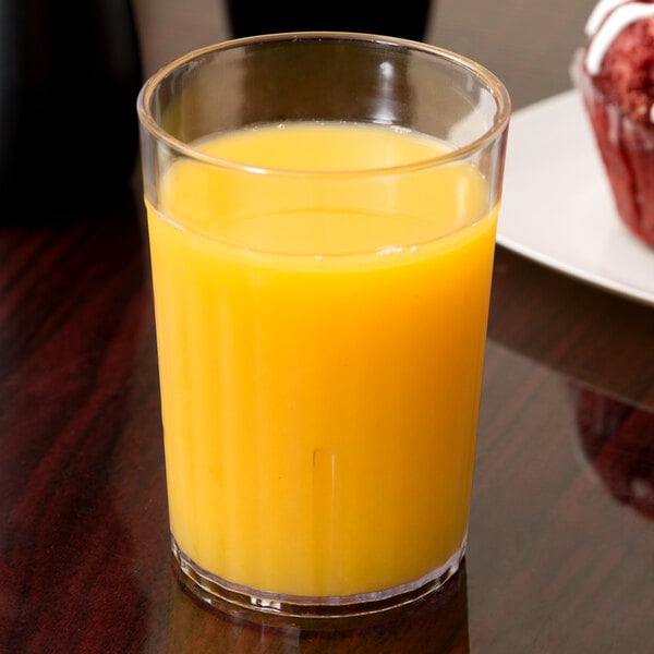 A Carlisle clear plastic tumbler filled with orange juice on a table.