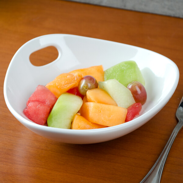 A Tuxton AlumaTux Pearl White china bowl filled with sliced fruit on a white table.
