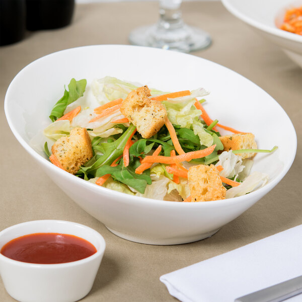 A bowl of salad with croutons and sauce on a table with a Tuxton AlumaTux Pearl White bowl.