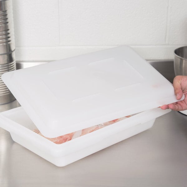 A person holding a white Cambro lid over a white plastic food storage box.