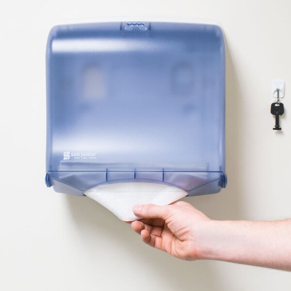 A hand holding a San Jamar Arctic Blue Ultrafold Fusion paper towel dispenser.