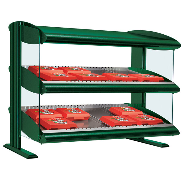 A green Hatco slanted double shelf merchandiser on a countertop with red boxes inside.