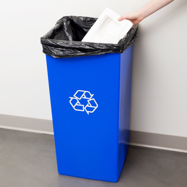 A hand putting a white bag into a blue Continental SwingLine recycling container.