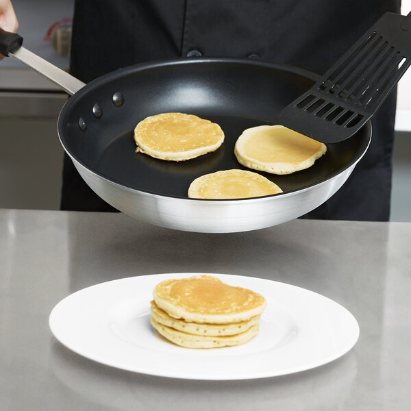 A person cooking a pancake in a Carlisle aluminum non-stick fry pan.