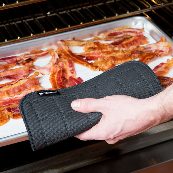 A person using a black San Jamar Ultigrips hot pad to hold a bacon pan.