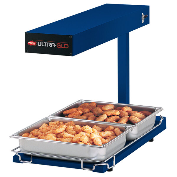 A blue tray of tater tots in a Hatco Ultra-Glo food warmer on a counter.