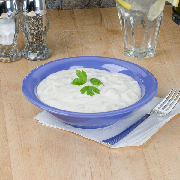 A purple melamine bowl filled with white sauce on a table with a fork and knife.