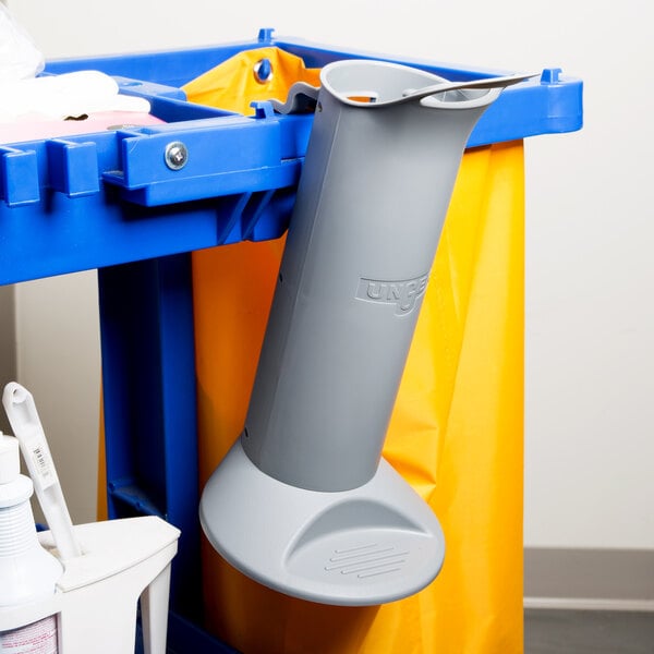 A grey plastic tube with a blue and yellow Unger toilet brush and swab holder on a white cart.