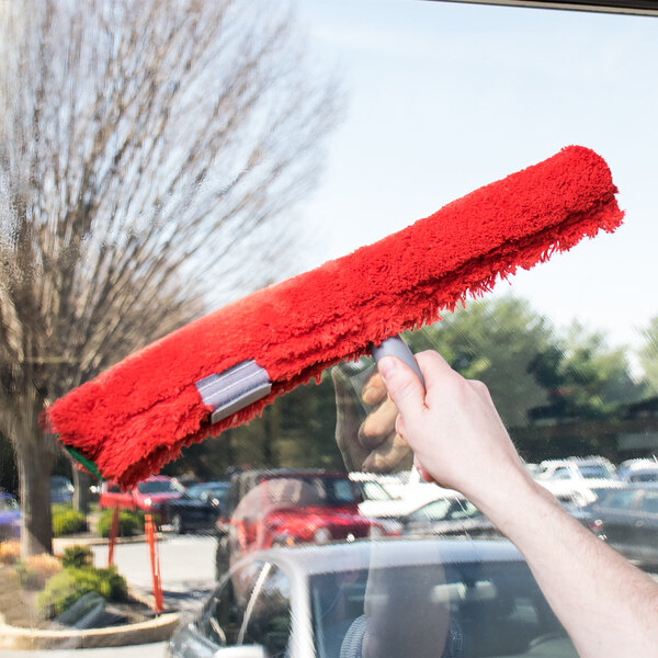 A hand using a red Unger Smart Color microfiber washer sleeve to clean a window.