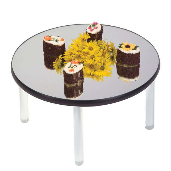 A Geneva round rimless mirror food display tray on a round glass table with cakes.