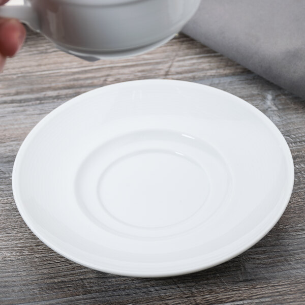 A hand holding an Arcoroc white cup over a bouillon saucer.