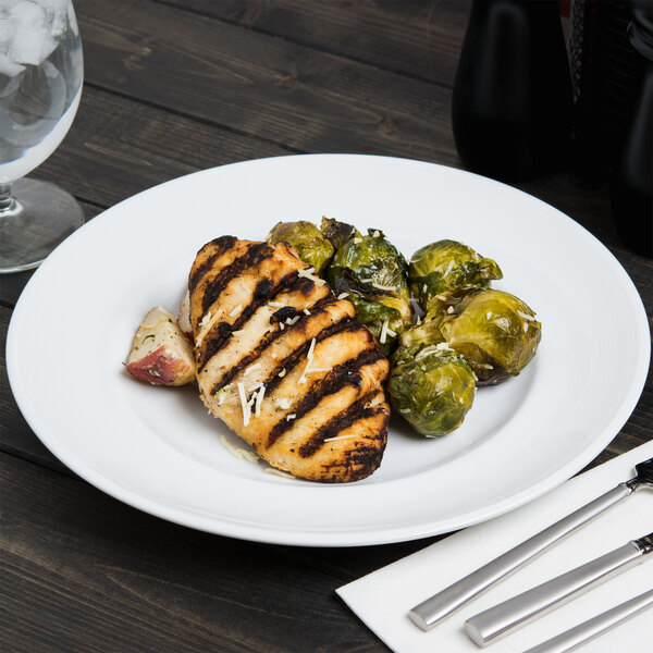 An Arcoroc Rondo dinner plate with chicken and brussels sprouts on a table.