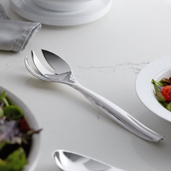 A Visions heavy weight silver plastic serving fork and a salad bowl on a table.