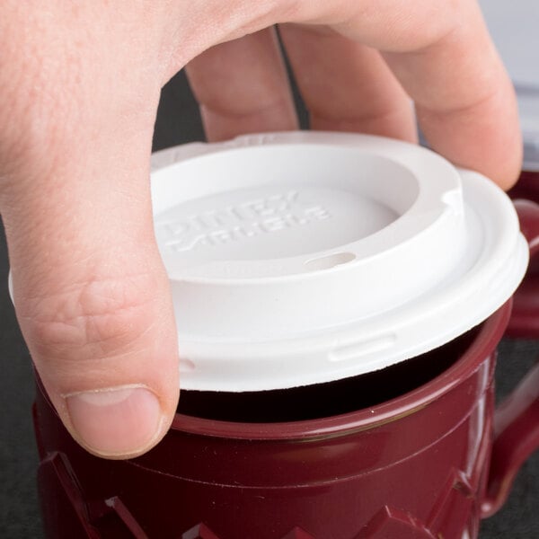 A hand placing a Fenwick translucent plastic lid on a coffee cup.