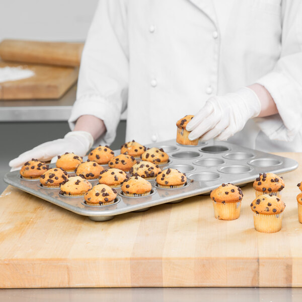 A person in white gloves holding a Chicago Metallic mini muffin pan filled with muffins.