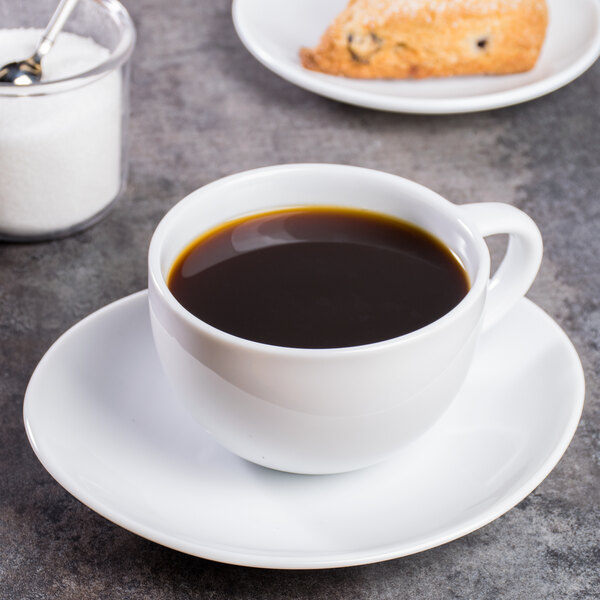 A white porcelain cup of coffee on a saucer with sugar on the side.