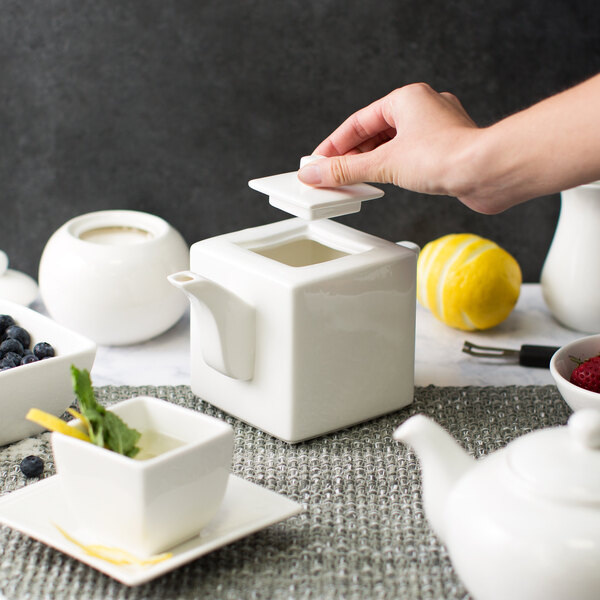 A hand putting a square lid on a white square teapot.