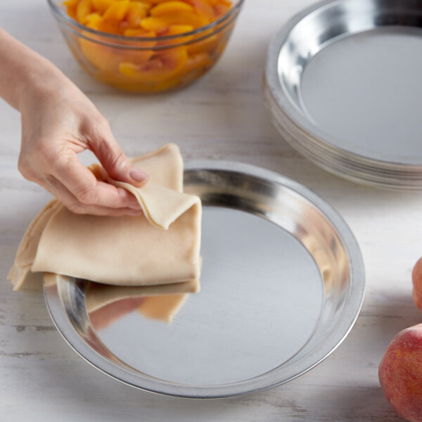 A hand using a cloth to wipe a Chicago Metallic tin-plated steel pie plate.