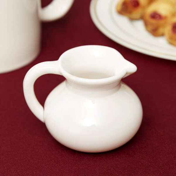 A white GET plastic creamer pitcher on a red surface.