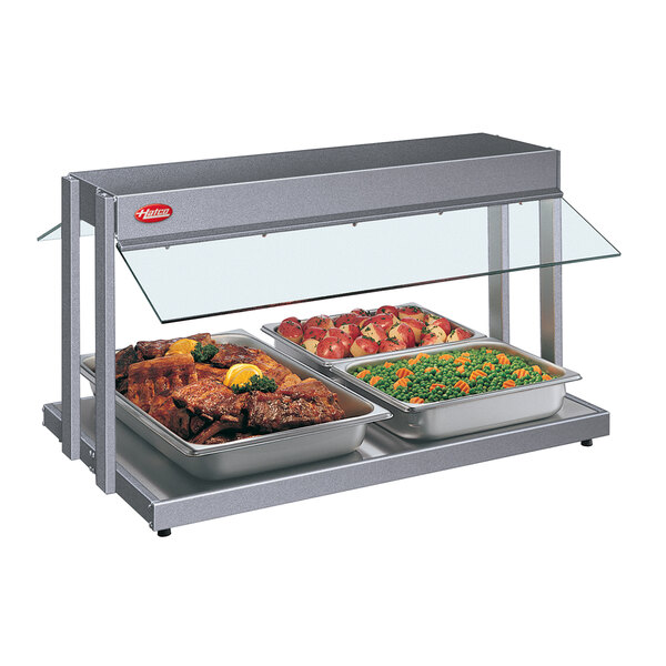 A Hatco countertop buffet warmer with trays of meat and vegetables on a table in a buffet.