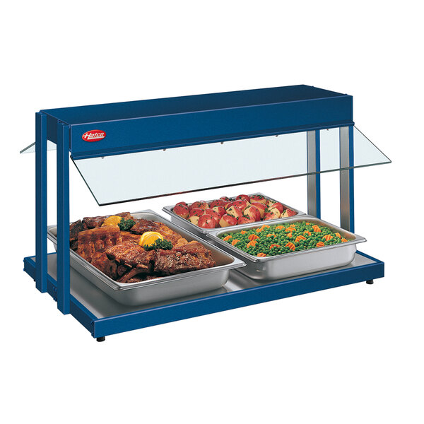 A navy blue Hatco buffet warmer with trays of food including peas, carrots, meat, and lemon wedges.