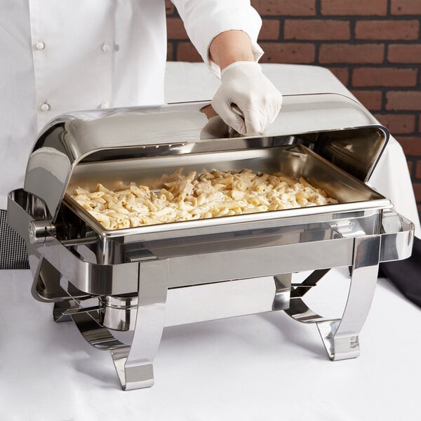 A person holding a Vollrath Orion Retractable Chafer full of food on an outdoor table.