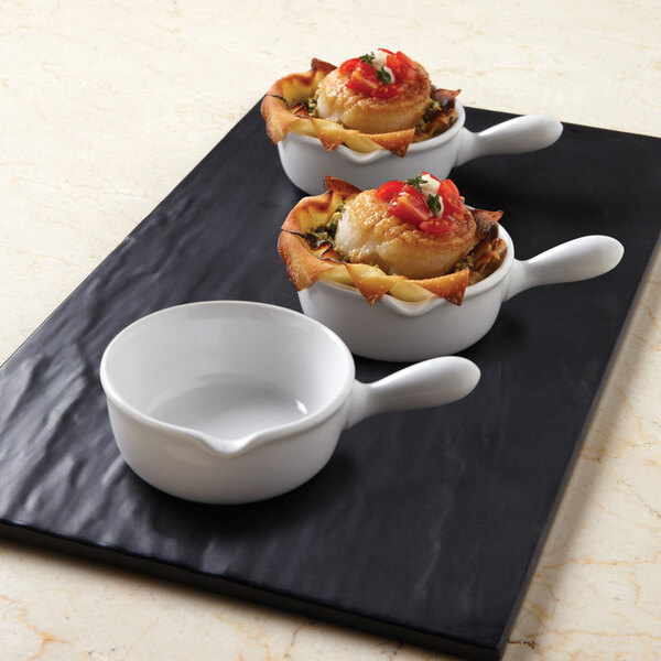 Three American Metalcraft mini ceramic fry pans with food in them on a black tray.