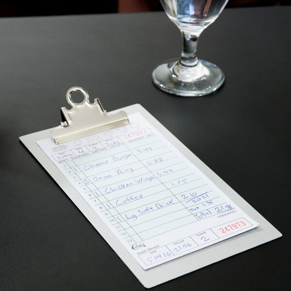 A green and white Choice guest check clipboard on a table with a glass of water.