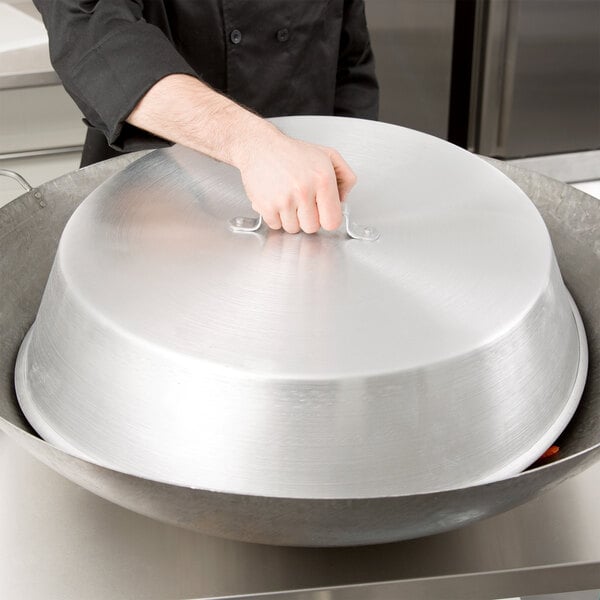 A hand holding a Town aluminum wok cover over a large metal wok.