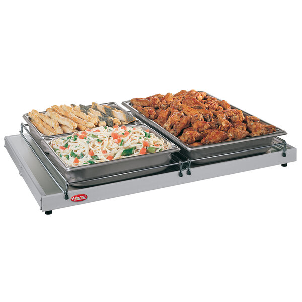 A Hatco portable heated shelf with trays of food on a table.