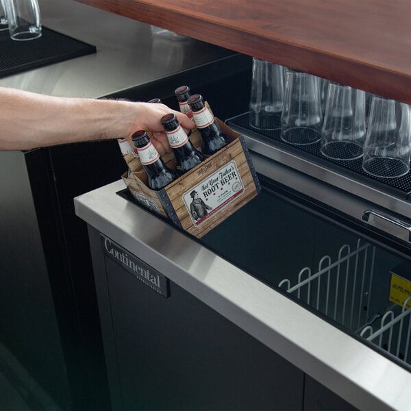 A hand holding a bottle of beer in a Continental bottle cooler.