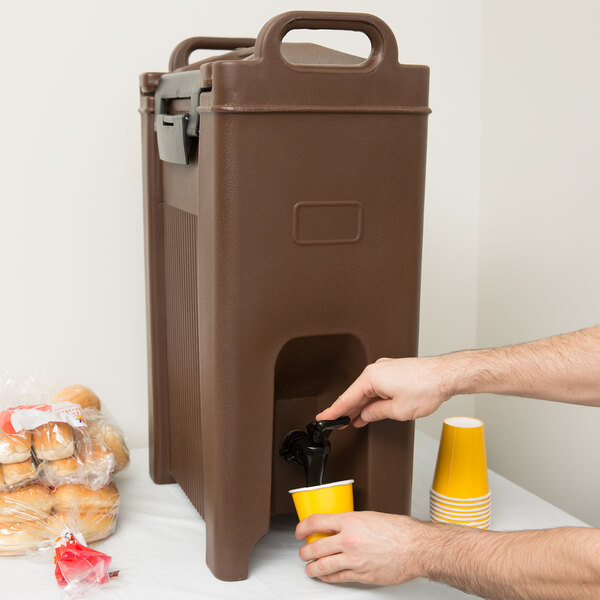 A man pouring coffee into a Carlisle brown insulated beverage dispenser.