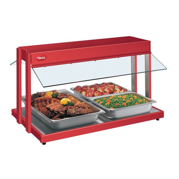 A Hatco red buffet warmer with trays of peas and carrots and meat with lemon wedges.