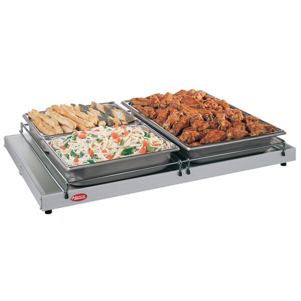 A Hatco heated shelf with trays of food on a table.