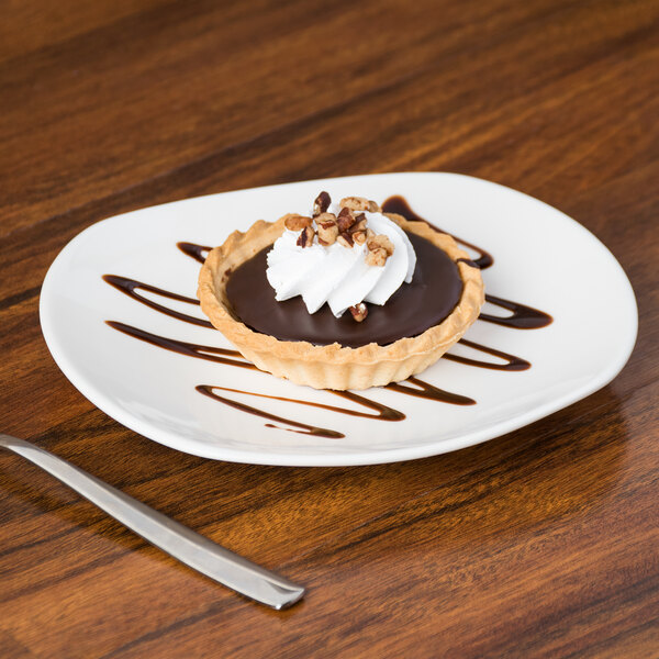 A small chocolate tart with whipped cream and nuts on a Tuxton AlumaTux Pearl White plate.